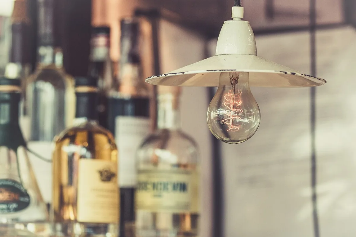 Hanglamp met een emaillen kap laag boven een blad met flessen